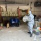 An investigator in a hazmat suit stands with paraphernalia suspected of use in making illicit drugs