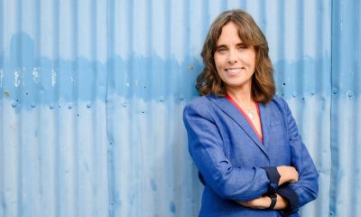 BC Green Party Leader Sonia Furstenau stands against a blue background with her arms crossed