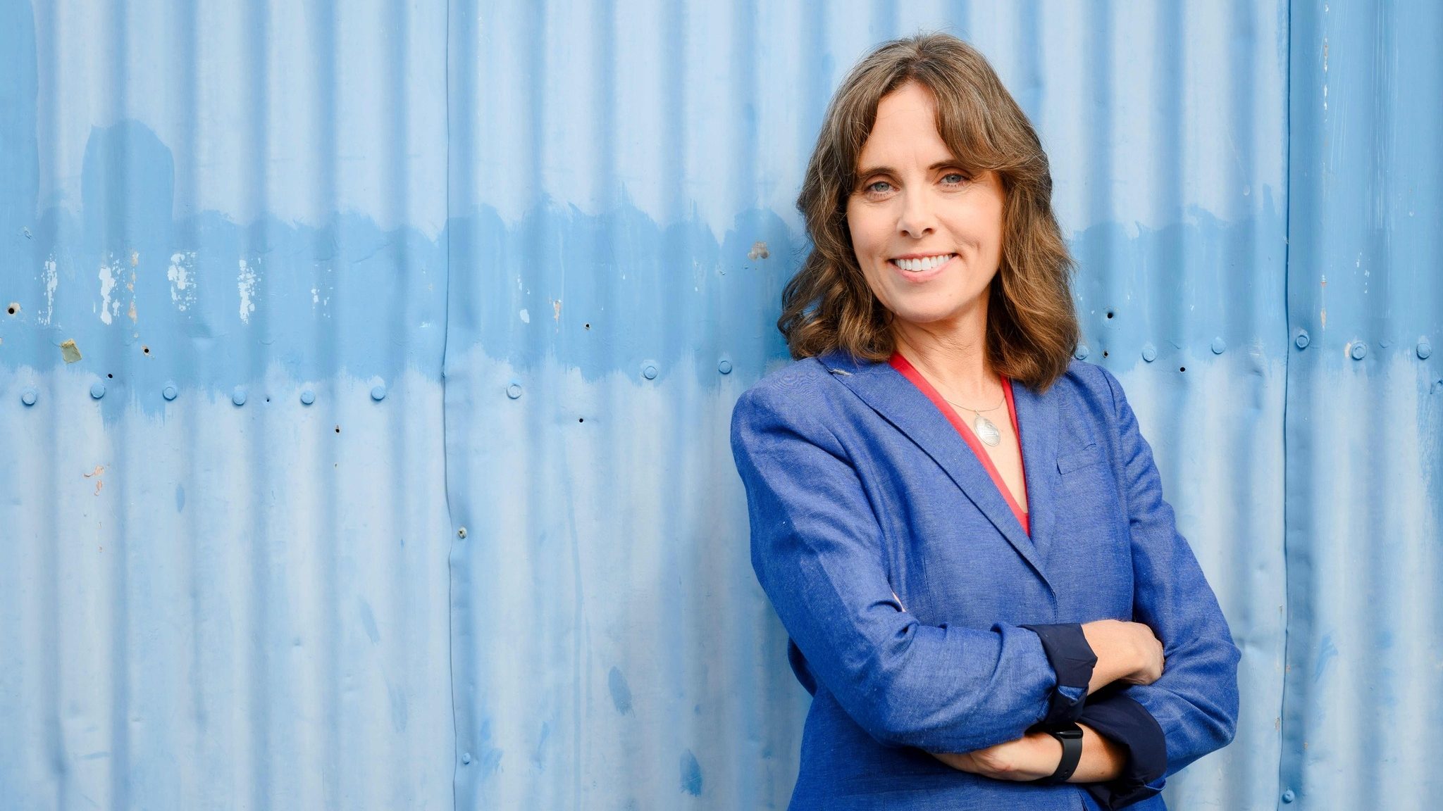 BC Green Party Leader Sonia Furstenau stands against a blue background with her arms crossed