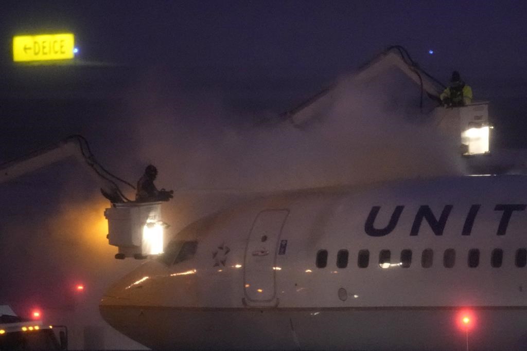 Workers brave near zero-degree weather and snow to spray deicer on a United Airlines jet Friday, Jan. 12, 2024