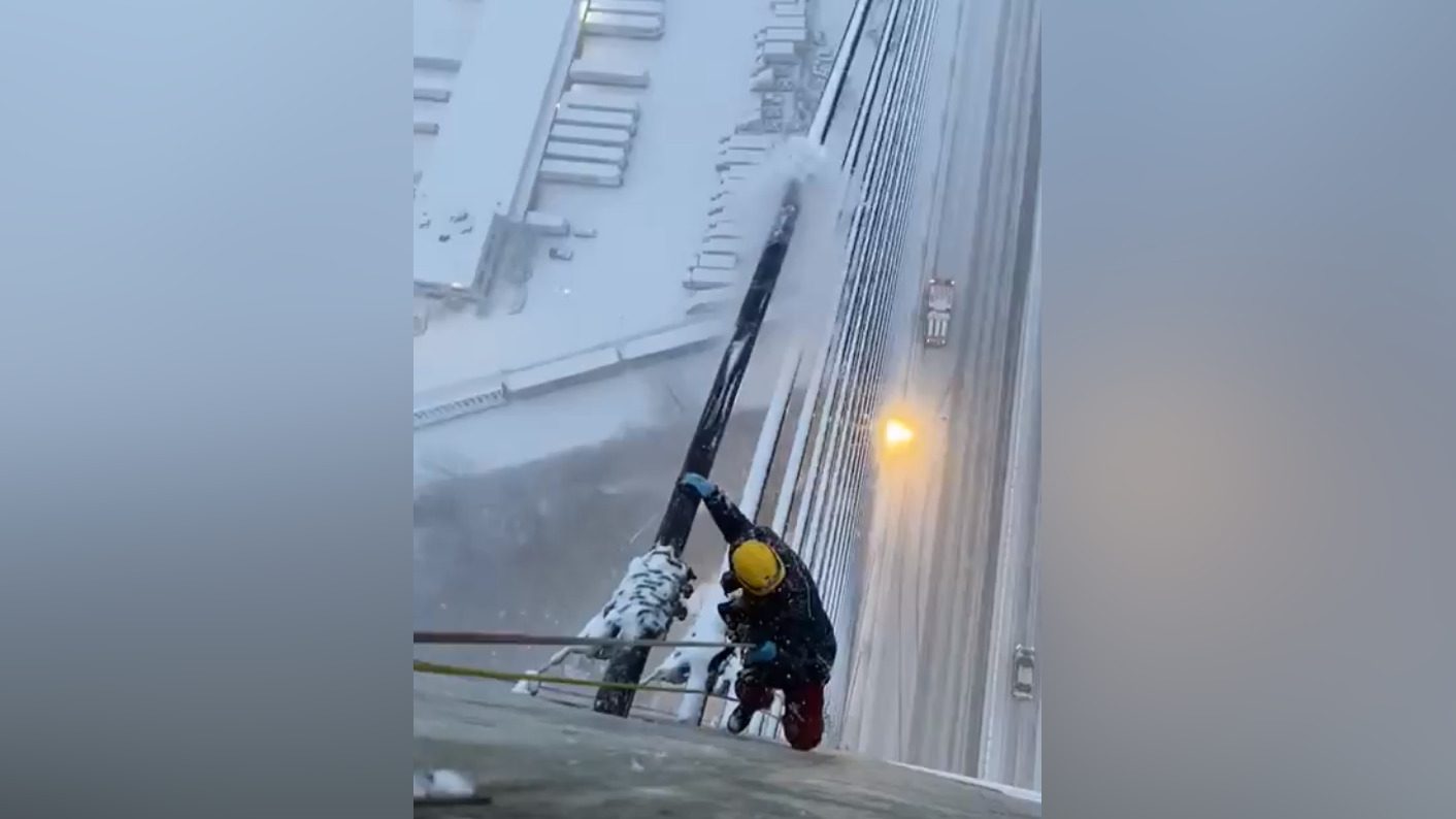 A Rope Access Technician (RAT) at the top of the Alex Fraser Bridge clears cables of ice and snow build up during a storm