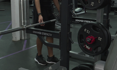 A person is seen at a gym lining up to use a squat rack, with a weight filled bar resting on the rack.