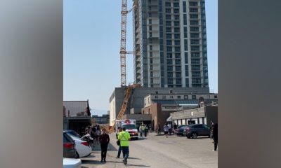 A crane is seen collapsed against a building in Kelowna as people look on from a distance