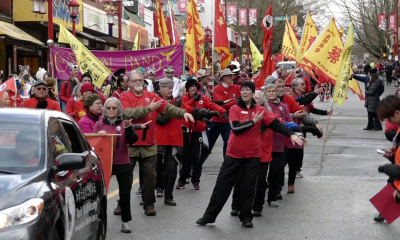 Image of Lunar New Year Parade in Vancouver Chinatown. People dressed in red with Lunar New Year signs stand in line at the parade.