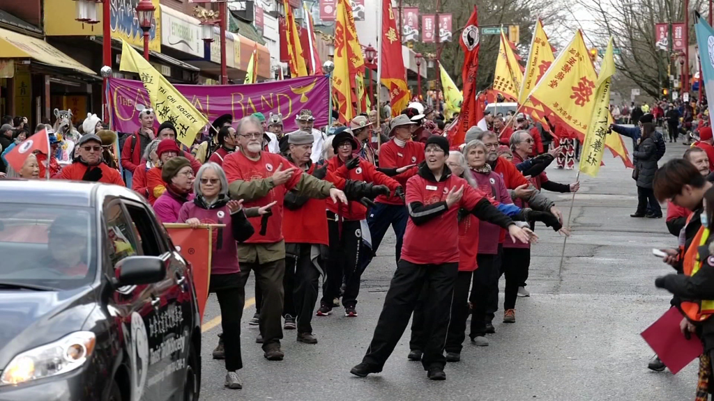 Image of Lunar New Year Parade in Vancouver Chinatown. People dressed in red with Lunar New Year signs stand in line at the parade.