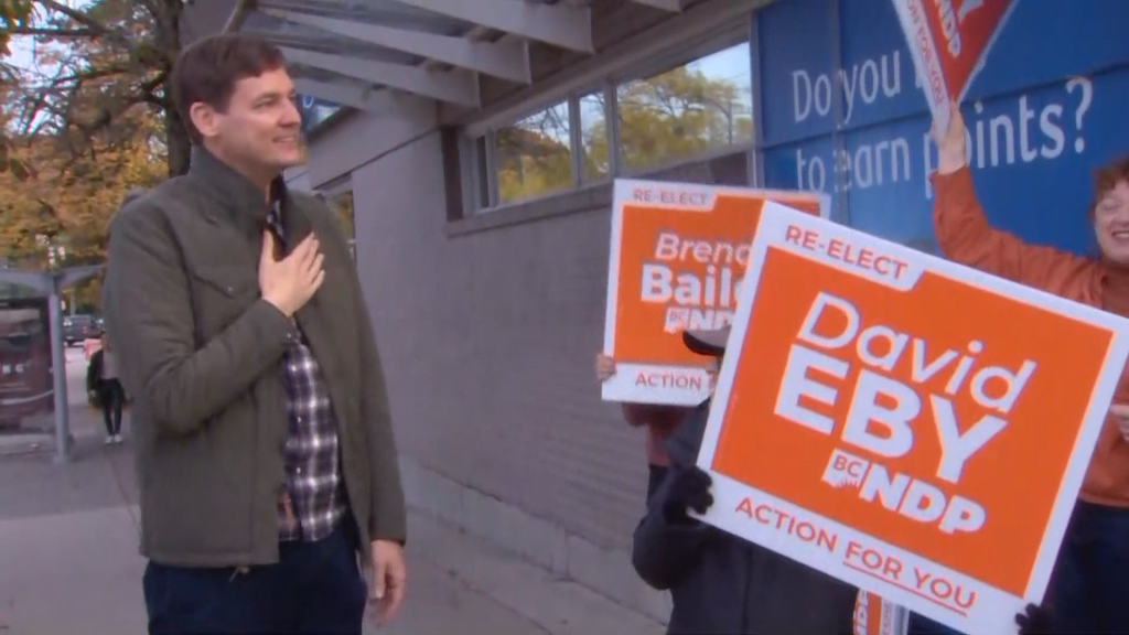 David eby speaks with people holding electoral signs