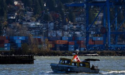 A water taxi travels on the Fraser River past cargo containers stacked at Fraser Surrey Docks below houses on a hill, in Surrey, B.C., on Monday, November 4, 2024. Business groups say the work stoppage at B.C. ports is the latest in a run of supply chain disruptions affecting Canadian companies and the country's economy.THE CANADIAN PRESS/Darryl Dyck