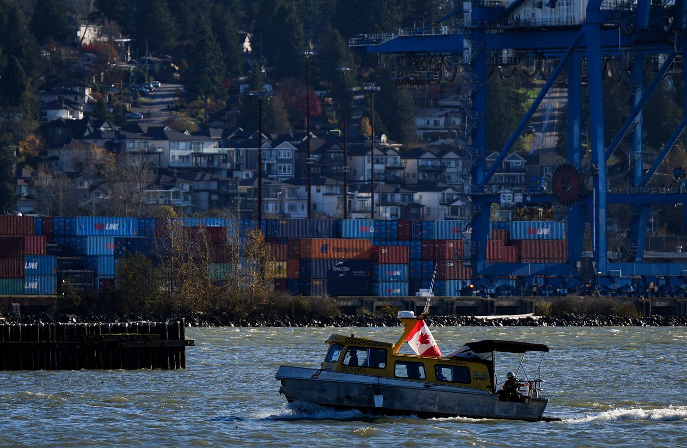 A water taxi travels on the Fraser River past cargo containers stacked at Fraser Surrey Docks below houses on a hill, in Surrey, B.C., on Monday, November 4, 2024. Business groups say the work stoppage at B.C. ports is the latest in a run of supply chain disruptions affecting Canadian companies and the country's economy.THE CANADIAN PRESS/Darryl Dyck