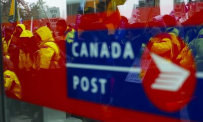 The strike by more than 55,000 Canada Post workers entered its 19th day as the Black Friday and Cyber Monday shopping weekend came to a close. Canada Post employees and supporters rally as they are reflected in a window at Canada Post headquarters in Ottawa, Thursday, Nov. 28, 2024.