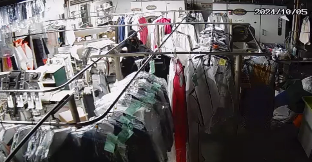 CCTV footage of a suspect in a balaclava stealing uniforms from a dry cleaner rack